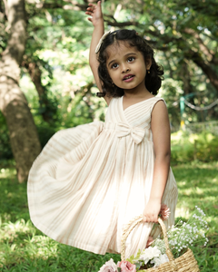 Young girl in the Faye Striped Beige Dress holding a basket of flowers in a natural setting.