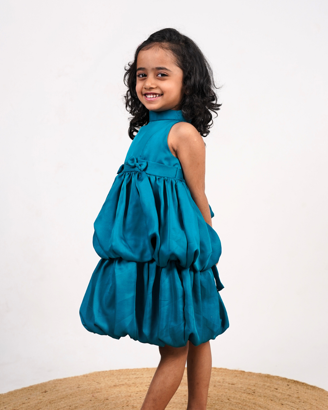 Faye Peacock Blue Tiered Dress with a halter neck, balloon hemline, and two bows on the waist.
