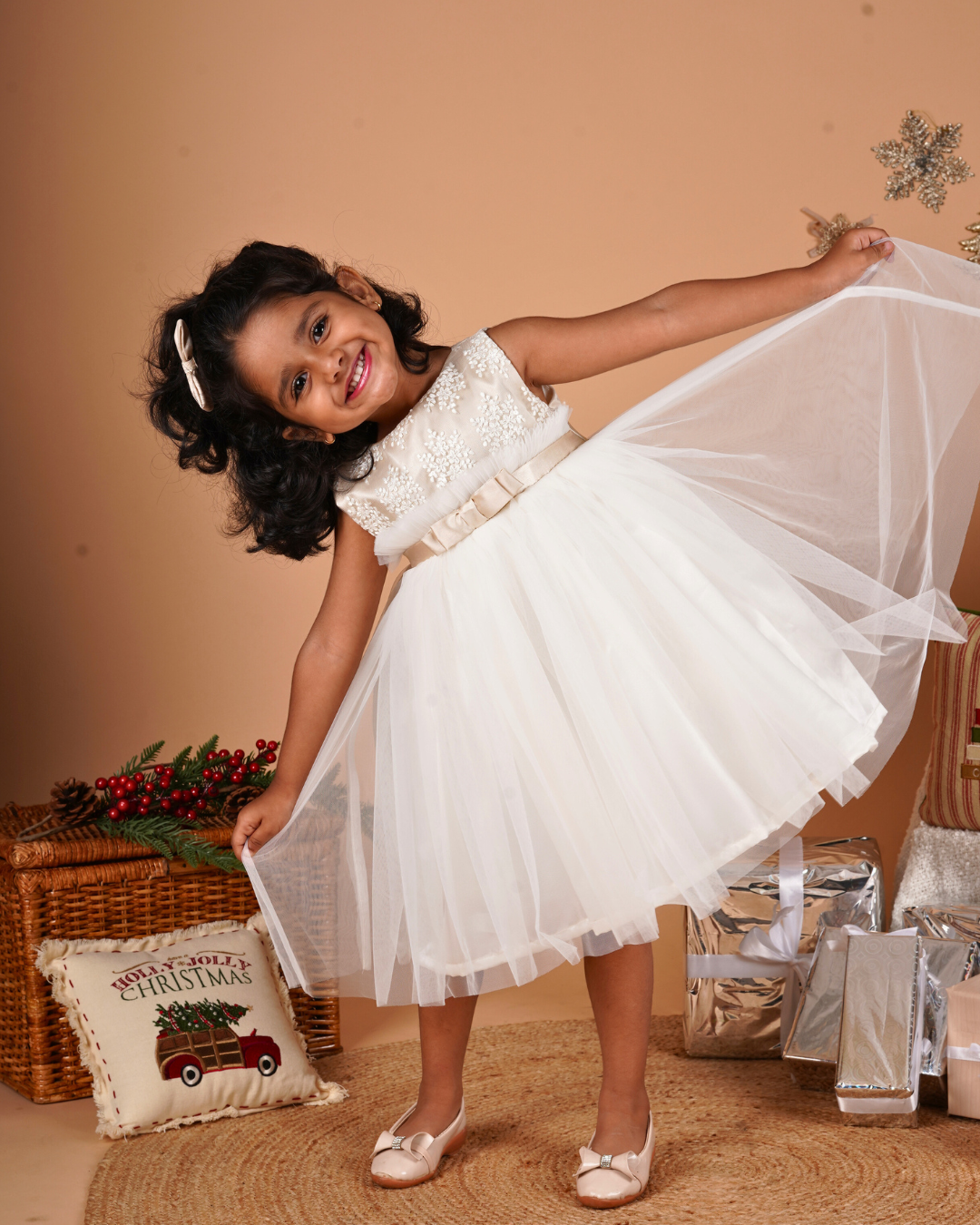 Young girl in the Faye Champagne and Ivory Frill Dress standing next to a Christmas decorations.