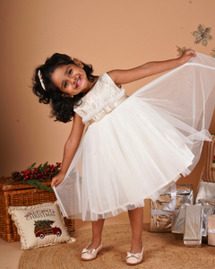 Young girl in the Faye Champagne and Ivory Frill Dress standing next to a Christmas decorations.