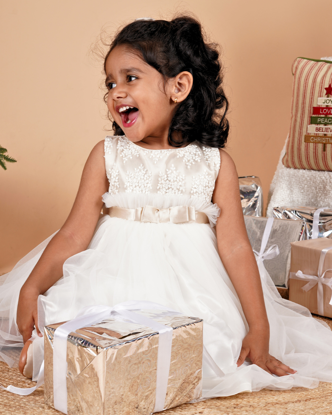 Young girl in the Faye Champagne and Ivory Frill Dress sitting next to a Christmas presents.