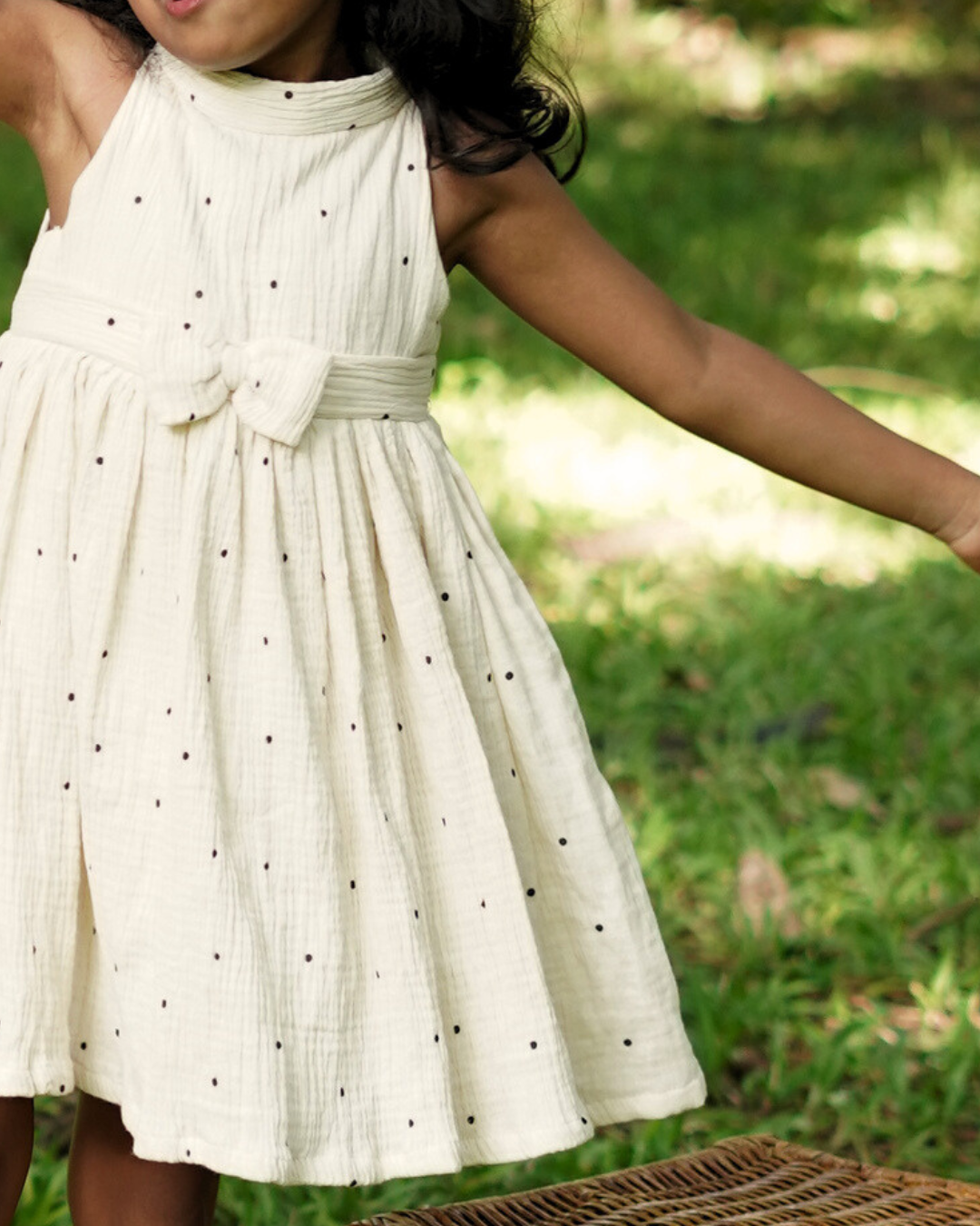Young girl wearing the Faye Cream Polka High-neck dress outdoors in a grassy area