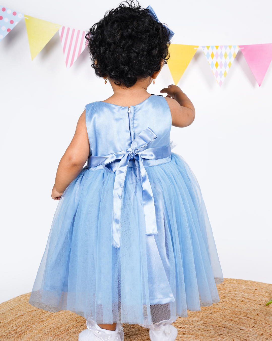 Child wearing the Faye Dusty Blue and Black V-Neck Dress with colorful flags in the background