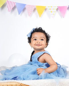 Child wearing the Faye Dusty Blue and Black V-Neck Dress with colorful flags in the background