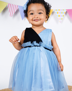 Child wearing the Faye Dusty Blue and Black V-Neck Dress with colorful flags in the background