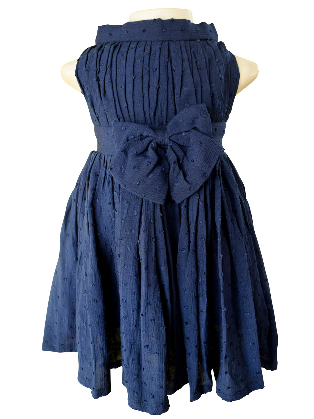 A sleeveless navy blue dress displayed on a  mannequin torso against a white background. The dress features a pleated bodice, a large matching bow at the waist, and a flared skirt with a subtle dotted texture.