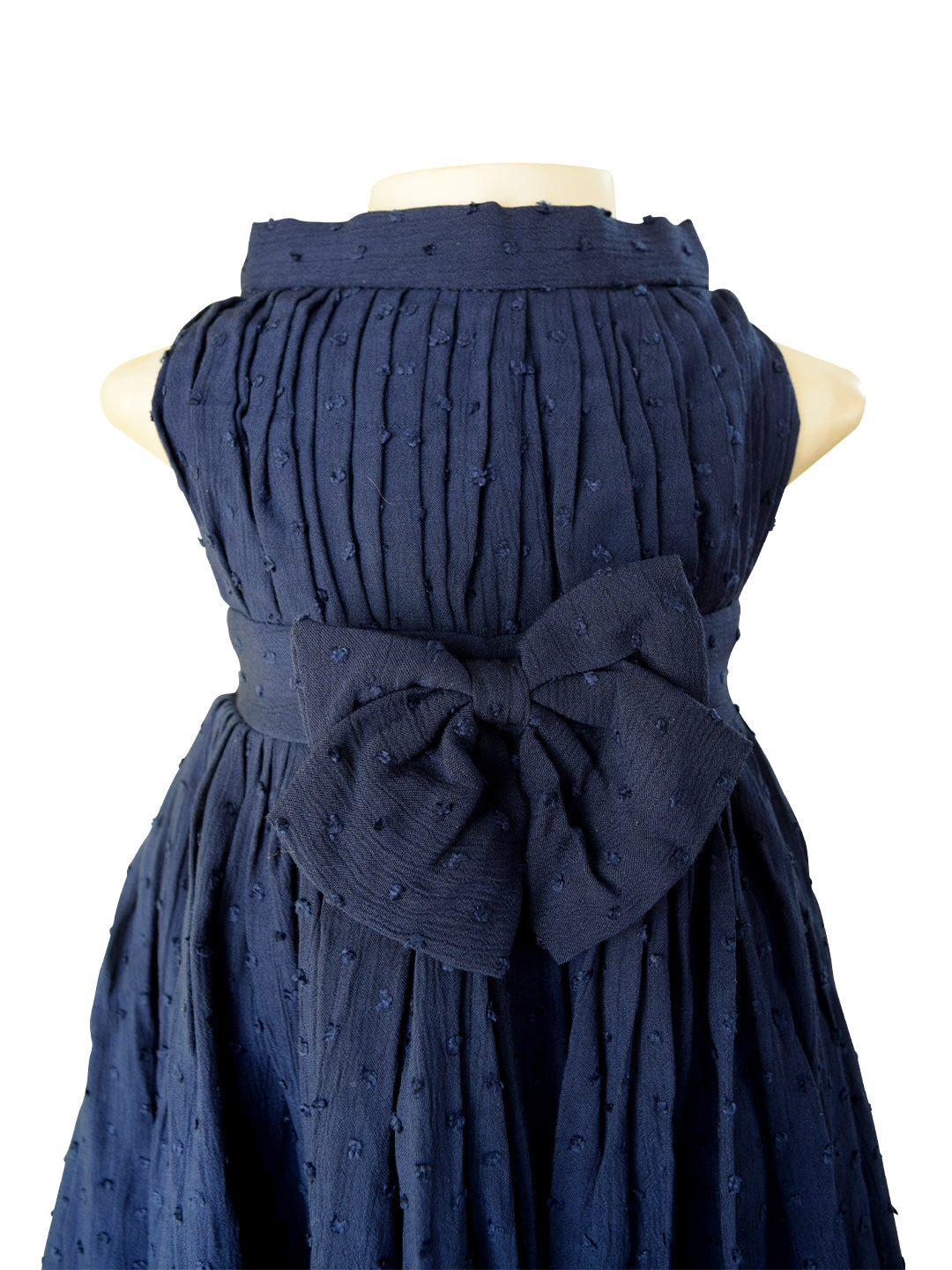 A sleeveless navy blue dress displayed on a cream mannequin torso against a plain white background. The dress features a textured, dotted fabric, a pleated bodice, and a large matching fabric bow at the waist.