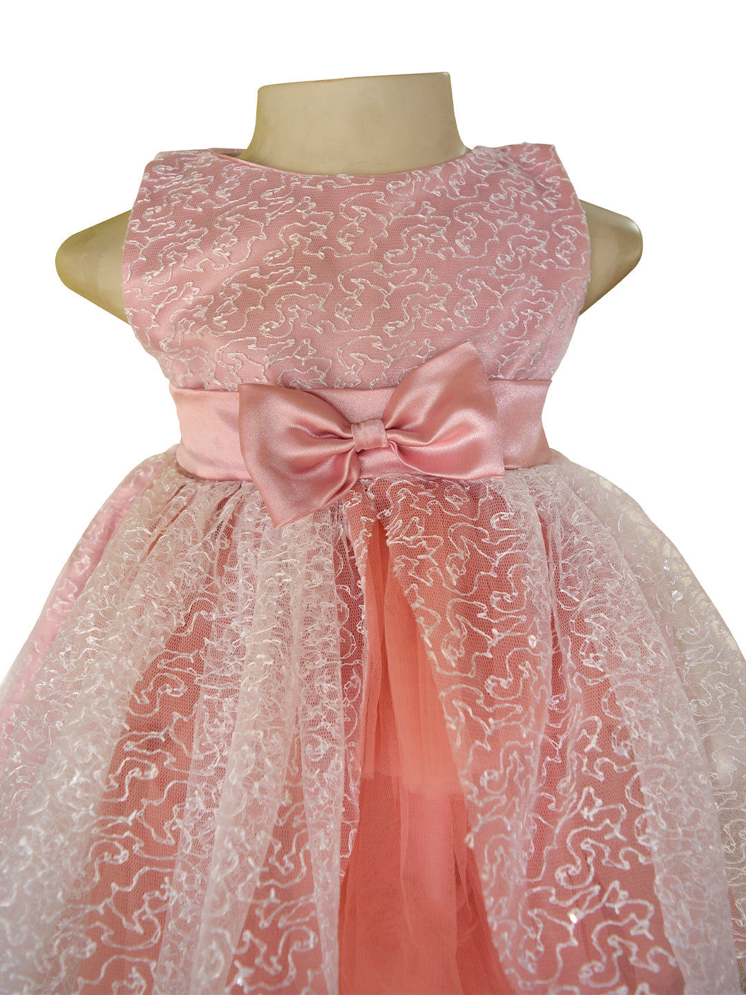 A pink sleeveless kids party dress from faye. The dress has a textured pink bodice with a matching satin bow at the waist, layered tulle, and a sheer floral lace overlay.
