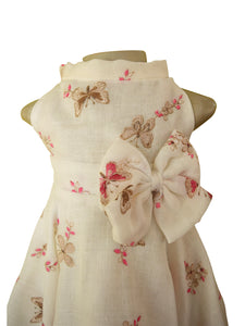 An off-white sleeveless dress displayed on a mannequin, featuring a large matching fabric bow with butterflies and pink floral printed details.