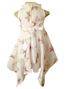 A sleeveless handkerchief dress displayed on a mannequin torso, featuring a cream base with a  butterfly and pink floral print pattern, shown from the back.