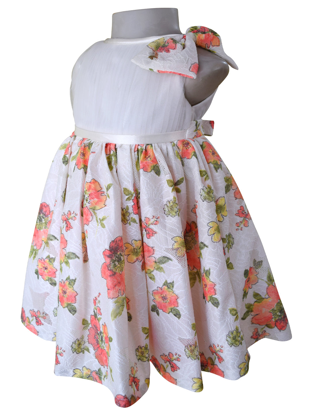 A sleeveless dress for baby girls  featuring a satin waistband, and a flared skirt with a coral and green floral print. A matching floral bow is attached to the shoulder.