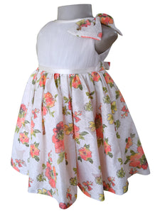 A sleeveless dress for baby girls  featuring a satin waistband, and a flared skirt with a coral and green floral print. A matching floral bow is attached to the shoulder.