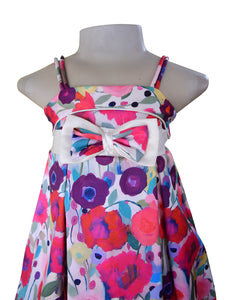 A girls' floral dress displayed on a mannequin against a white background. The dress has thin shoulder straps, a large double bow at the waist, and a colorful watercolor-style floral print with pink, purple, red, blue, and green tones.