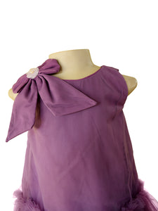 A sleeveless purple dress. The dress features a large bow on the shoulder with a small white flower accent and a ruffled tulle hem.