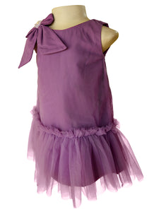 A sleeveless toddler girl's dress in dusty purple, displayed on a mannequin. The dress features a large bow detail on the shoulder, a ruffled tulle hem, and a tiered tulle skirt.