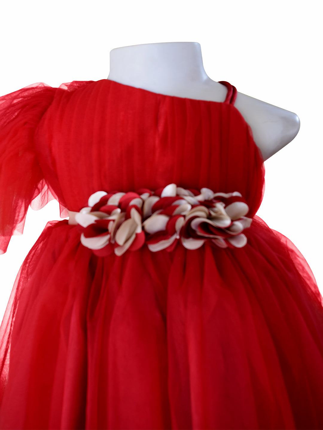 A bright maroon tulle dress. The dress features a one-shoulder design with a large decorative floral waistband made of alternating maroon & gold fabric petals.