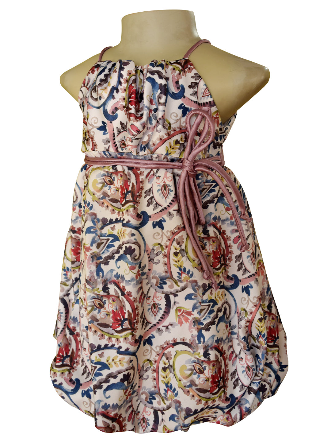 A sleeveless halter dress displayed on a mannequin torso against a plain white background. The dress has an allover paisley-style print with a cream base and multicolored motifs in blue, red, green, and yellow, accented by a mauve pink tie belt at the waist.