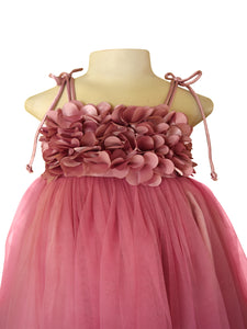 A mauve pink girl's party dress from faye. The dress features a voluminous tulle skirt and a textured bodice composed of layered, fabric flower petals with thin tie-shoulder straps.