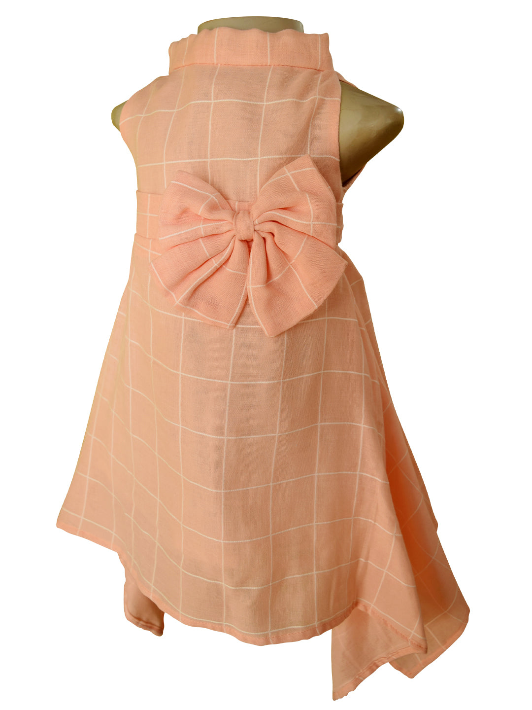 A sleeveless peach-colored dress displayed on a mannequin, featuring a large matching fabric bow and a white windowpane plaid pattern.