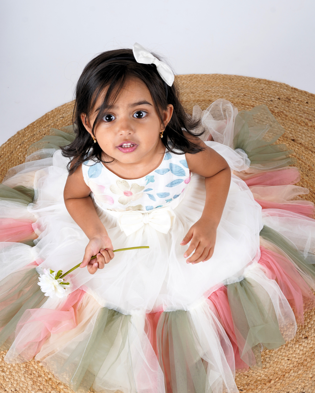 Young girl in the Faye Embroidered Tiered Multi-coloured Pastel Dress sitting on a woven mat.